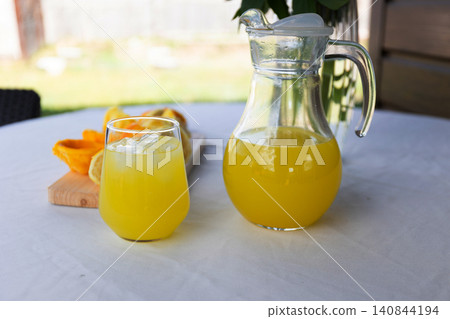 Glass pitcher and glass of fresh orange juice on outdoor table with sliced fruit Glass pitcher and glass of fresh orange juice on outdoor table with sliced fruit 140844194