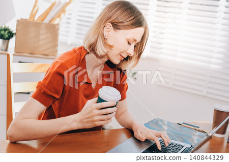 Young woman works on a touchpad, feeling comfortable at cozy home office with a green plant on the background Young woman works on a touchpad, feeling comfortable at cozy home office with a green plant on the background 140844329