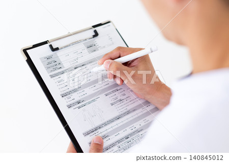 A middle-aged male acupuncturist/osteopath in a white coat filling out a medical questionnaire. A middle-aged male acupuncturist/osteopath in a white coat filling out a medical questionnaire. 140845012