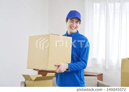 A smiling moving company worker holding cardboard boxes. 140845072