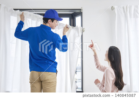 The moving company installs the curtains while a woman gives instructions. The moving company installs the curtains while a woman gives instructions. 140845087