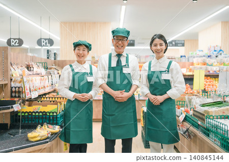 三位面帶微笑的店員在超市的蔬果區排成一排。 三位面帶微笑的店員在超市的蔬果區排成一排。 140845144