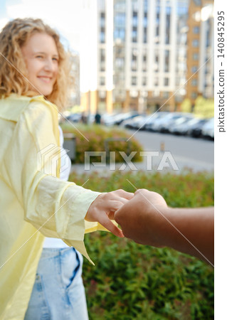 Couple walking hand in hand through urban area with buildings and cars in background Couple walking hand in hand through urban area with buildings and cars in background 140845295