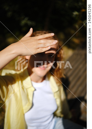 Woman shielding eyes from sunlight while sitting outdoors in a relaxed setting during daytime Woman shielding eyes from sunlight while sitting outdoors in a relaxed setting during daytime 140845296