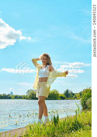 Woman stands by water in sunny location with blue sky and clouds during warm afternoon 140845323
