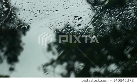 Rainwater Streaming Down Glass Window Pane - Moody Heavy Rain Drops Texture with Blurred Dark Green Trees and Overcast Sky, Melancholy Rainy Day Background Rainwater Streaming Down Glass Window Pane - Moody Heavy Rain Drops Texture with Blurred Dark Green Trees and Overcast Sky, Melancholy Rainy Day Background 140845378
