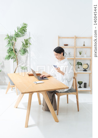 A woman using her smartphone and laptop in her room. (Keywords: apps, freelance, work, lifestyle, DX) A woman using her smartphone and laptop in her room. (Keywords: apps, freelance, work, lifestyle, DX) 140845441