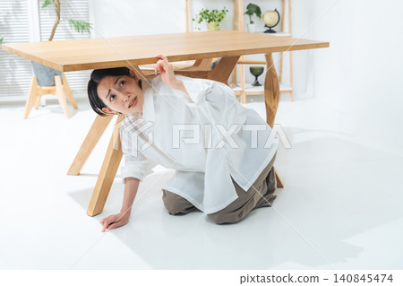 一名女子躲在桌子底下。地震、災難、疏散、防災、驚訝、害怕、恐怖、地震警報。 140845474