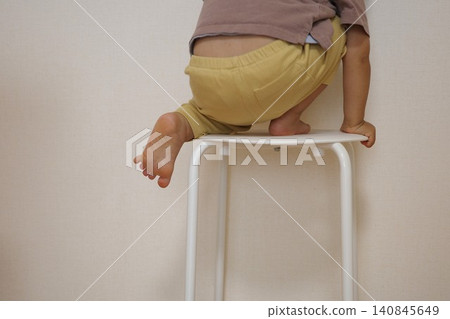 危險的幼兒爬上屋裡的椅子時,從背後拍攝的畫面。 危險的幼兒爬上屋裡的椅子時,從背後拍攝的畫面。 140845649