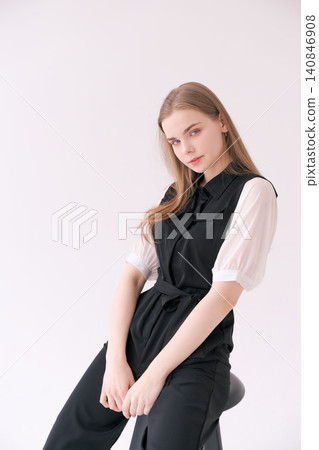 Serene Young Woman Sitting on a Stool in a Black Jumpsuit Studio Serene Young Woman Sitting on a Stool in a Black Jumpsuit Studio 140846908