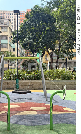 Urban playground with tire swing and colorful safety surfacing near apartment buildings 140846952