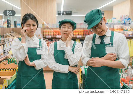 Three staff members looking dejected and sad in the supermarket aisle. Three staff members looking dejected and sad in the supermarket aisle. 140847125