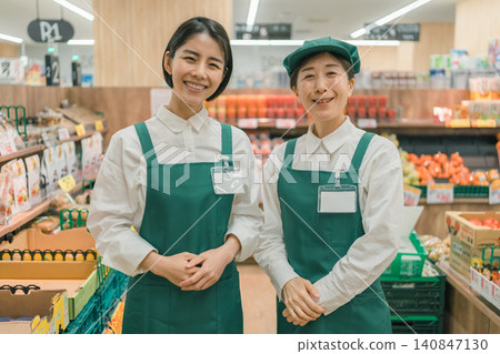 Two female store clerks smiling in the produce section of a supermarket. Two female store clerks smiling in the produce section of a supermarket. 140847130
