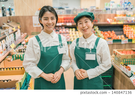 A young and veteran employee smiling in the produce section of a supermarket. A young and veteran employee smiling in the produce section of a supermarket. 140847136