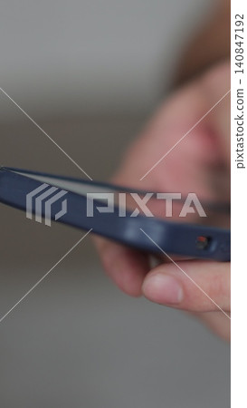 Vertical video Close up of hands of man writes a text message on smartphone in the living room at home. Online shopping in social media. Vertical video Close up of hands of man writes a text message on smartphone in the living room at home. Online shopping in social media. 140847192