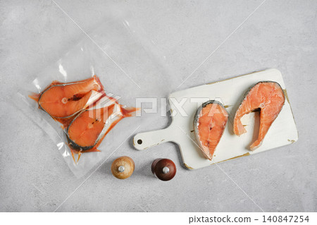 Unpacked slices of salmon steaks on cutting board alongside with fish fillets in vacuum sealed bag Unpacked slices of salmon steaks on cutting board alongside with fish fillets in vacuum sealed bag 140847254
