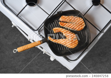 Grilling salmon fillets on stovetop with grill pan in kitchen Grilling salmon fillets on stovetop with grill pan in kitchen 140847258