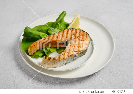 Grilled salmon steak on white plate next to fresh salad leaves and slice of lemon on white plate Grilled salmon steak on white plate next to fresh salad leaves and slice of lemon on white plate 140847261