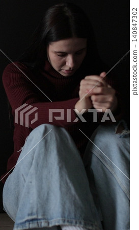 Vertical video Sad woman sitting in the dark leaning against the wall in home. Domestic violence, family problems, stress, violence. Vertical video Sad woman sitting in the dark leaning against the wall in home. Domestic violence, family problems, stress, violence. 140847302
