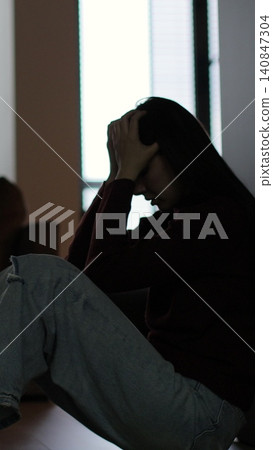 Vertical video Silhouette of a sad woman sitting in the dark leaning against the wall in home. Domestic violence, family problems, stress, violence. 140847304