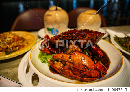 SINGAPORE - JUNE 30, 2025: A traditional Singaporean black pepper crab dish served in a large bowl alongside fresh chilled young coconuts on a table SINGAPORE - JUNE 30, 2025: A traditional Singaporean black pepper crab dish served in a large bowl alongside fresh chilled young coconuts on a table 140847845