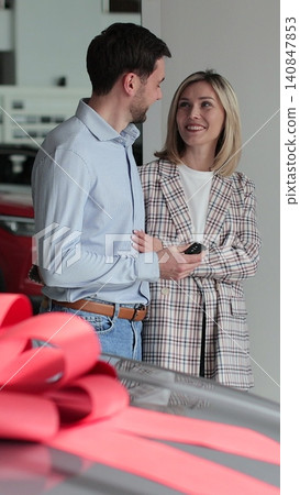 Vertical video Young couple buying new car in car dealership. Saleswoman giving car keys to new car happy couple family buyers. Auto business concept. 140847853