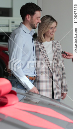 Vertical video Young couple buying new car in car dealership. Saleswoman giving car keys to new car happy couple family buyers. Auto business concept. 140847856