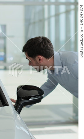 Vertical video Handsome man touching new car in showroom. Concept of car shopping, buying, and dealership. Vertical video Handsome man touching new car in showroom. Concept of car shopping, buying, and dealership. 140847874