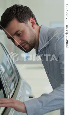 Vertical video Portrait of handsome man touching new car in showroom. Concept of car shopping, buying, and dealership. Vertical video Portrait of handsome man touching new car in showroom. Concept of car shopping, buying, and dealership. 140847875