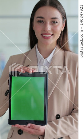 Vertical video Happy woman in a business suit, a manager at a car dealership holds a TabletPC with green screen in her hands and poses near the cars. Vertical video Happy woman in a business suit, a manager at a car dealership holds a TabletPC with green screen in her hands and poses near the cars. 140847923