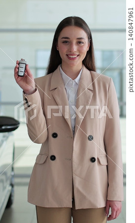 Vertical video Professional car saleswoman holding car keys standing near new cars at the dealership. Concept of car shopping, buying, and dealership. 140847961