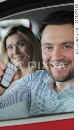 Vertical video Young man showing key to new car. Happy couple family buyers clients. Auto business concept. Man holding car keys at the dealership salon. Vertical video Young man showing key to new car. Happy couple family buyers clients. Auto business concept. Man holding car keys at the dealership salon. 140847988