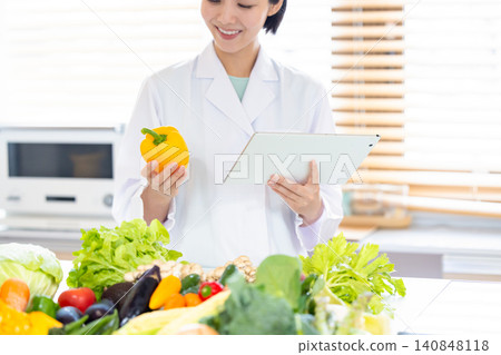Registered dietitian: A dietitian looking at a tablet in front of a large pile of vegetables. Registered dietitian: A dietitian looking at a tablet in front of a large pile of vegetables. 140848118