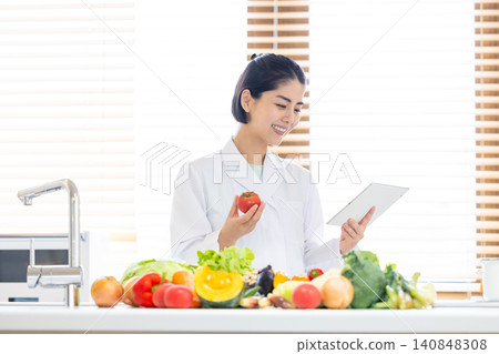 Registered dietitian: A dietitian looking at a tablet in front of a large pile of vegetables. Registered dietitian: A dietitian looking at a tablet in front of a large pile of vegetables. 140848308
