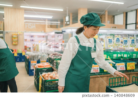 A female employee in her 50s working with her head down in the vegetable section of a supermarket. A female employee in her 50s working with her head down in the vegetable section of a supermarket. 140848609