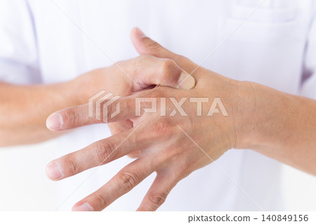 A middle-aged male acupuncturist/osteopath in a white coat presses the Hegu acupoint on the hand, which is effective for stomach pain. A middle-aged male acupuncturist/osteopath in a white coat presses the Hegu acupoint on the hand, which is effective for stomach pain. 140849156