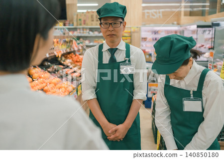 超市裡，一男一女兩名店員向顧客鞠躬。 140850180