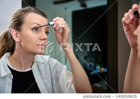 Woman applying mascara in mirror Woman applying mascara in mirror 140850620