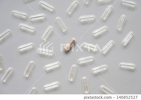 One filled medicine capsule surrounded by empty clear pills on gray background. 140852527