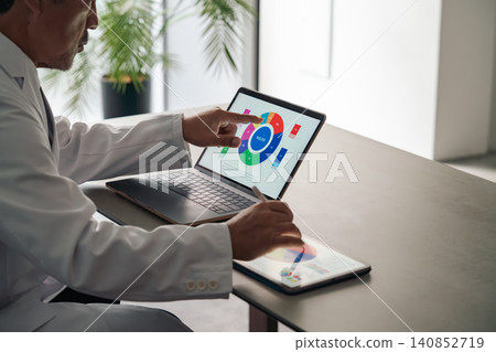 A man in a white coat working with a laptop and a tablet PC. (Medical, scientific, research, development, DX, IT) A man in a white coat working with a laptop and a tablet PC. (Medical, scientific, research, development, DX, IT) 140852719