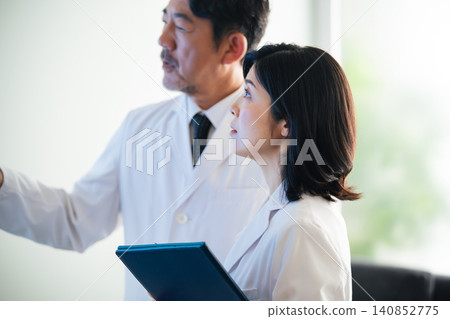 一群男女醫生一邊看著螢幕一邊交談。 （相關主題：醫療保健、檢查、治療、諮詢、會議） 140852775