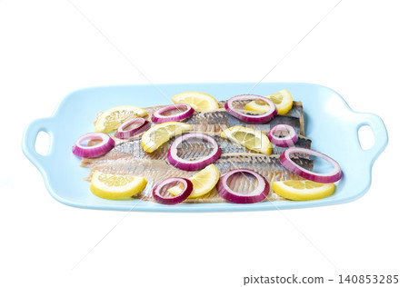 herring fillet with red onion rings and lemon on a blue plate isolated on a white background. herring fillet with red onion rings and lemon on a blue plate isolated on a white background. 140853285