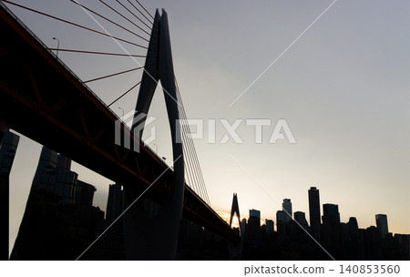 the structural geometry of the Qiansimen Bridge is reduced to a powerful silhouette, its soaring cables and monumental pylon boldly contrasting with the distant, block-like contours of a darkening 140853560