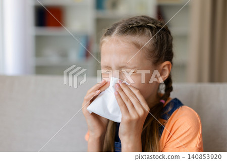 Teen girl blowing her nose with tissue at home, showing cold symptoms Teen girl blowing her nose with tissue at home, showing cold symptoms 140853920