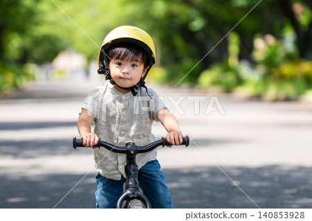 A boy wearing a helmet riding a balance bike A boy wearing a helmet riding a balance bike 140853928