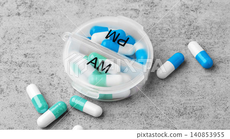 Capsule pills with am pm pill organizer box on a grey concrete background Capsule pills with am pm pill organizer box on a grey concrete background 140853955