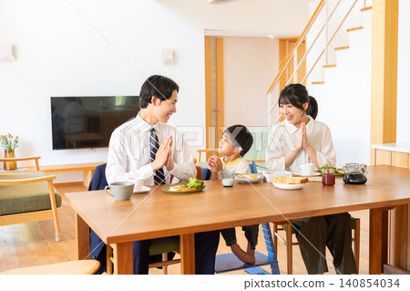 A family of three smiles and clasps their hands together before breakfast. 140854034