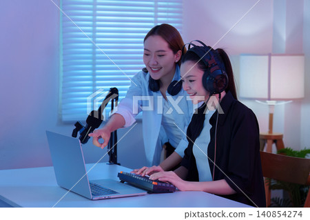 Two Asian women editing video and recording podcast on laptop in home studio Two Asian women editing video and recording podcast on laptop in home studio 140854274