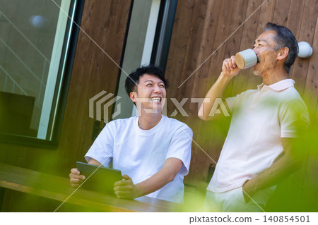 A senior father and son discuss the future while looking at a tablet on the terrace. A senior father and son discuss the future while looking at a tablet on the terrace. 140854501