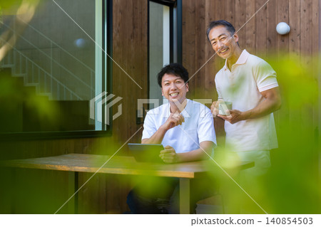 一對年邁的父親和兒子在露台上一邊看著平板電腦一邊討論未來。 一對年邁的父親和兒子在露台上一邊看著平板電腦一邊討論未來。 140854503